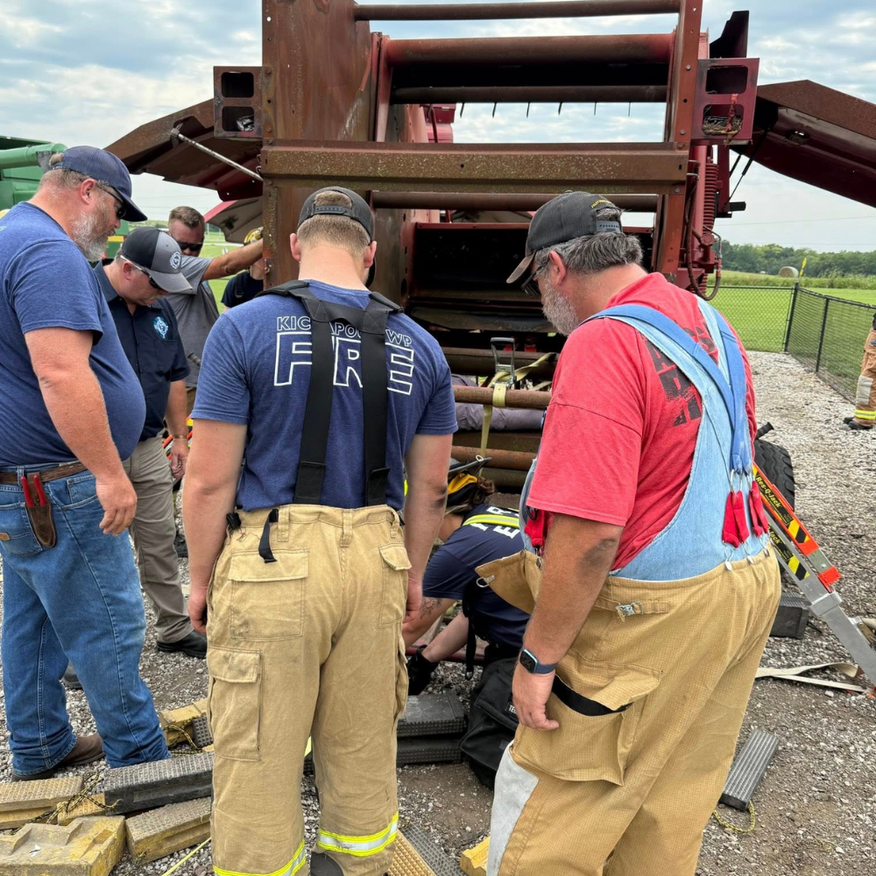 Firefighters assisting someone trapped in farm machinery. Outdoors, daylight.