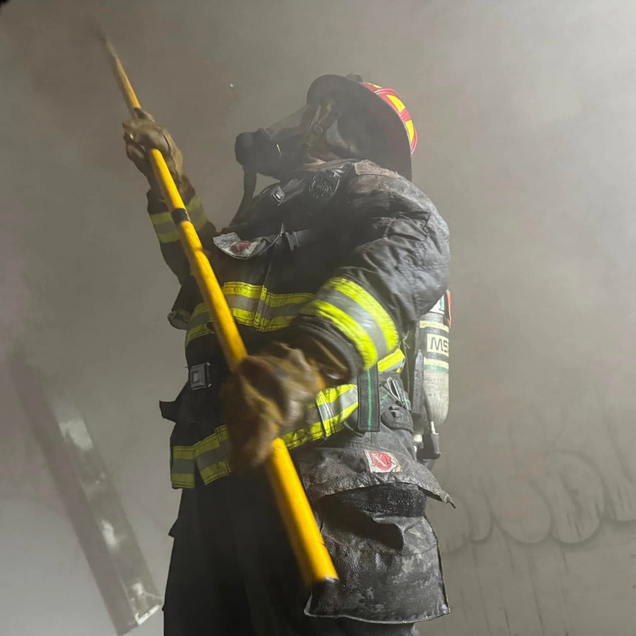 Firefighter in yellow-striped gear holding a yellow tool amid heavy smoke.