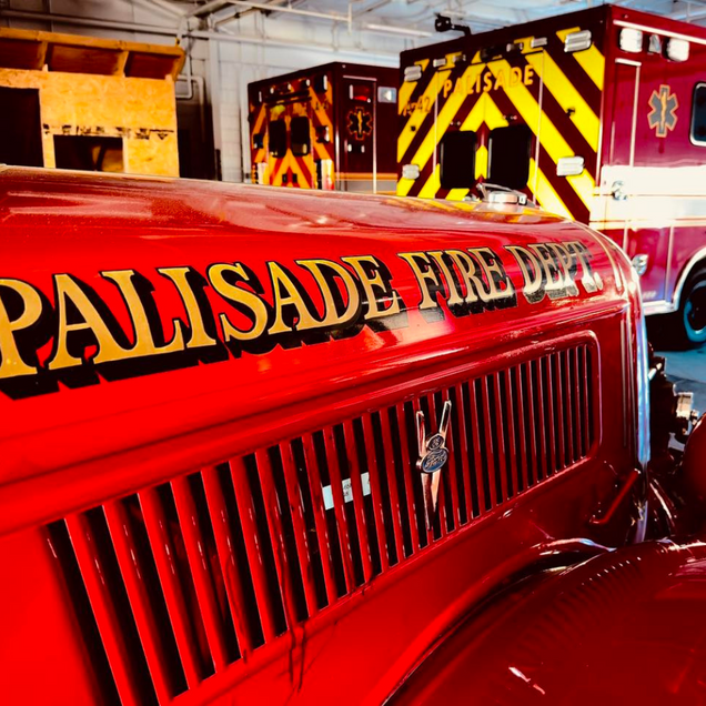 Red Palisade fire department truck in a fire station bay with emergency vehicle stripes in the background