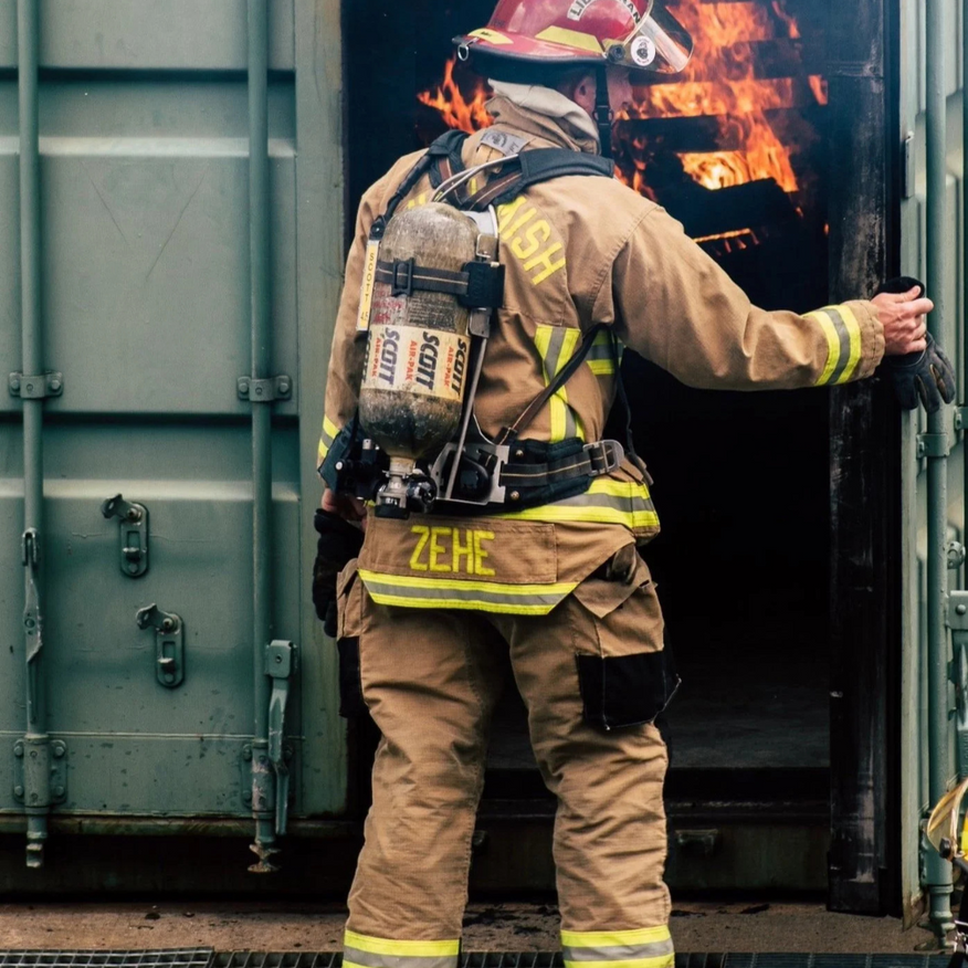 Firefighter in tan gear opens a container door with flames inside