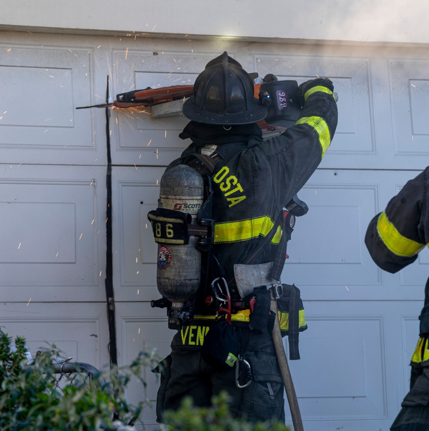Firefighter using a saw on a garage door, sparks flying.
