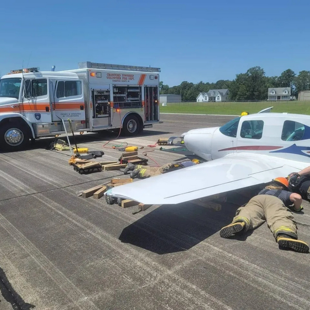 Emergency responders beside a small plane on a runway, with a fire truck and equipment nearby