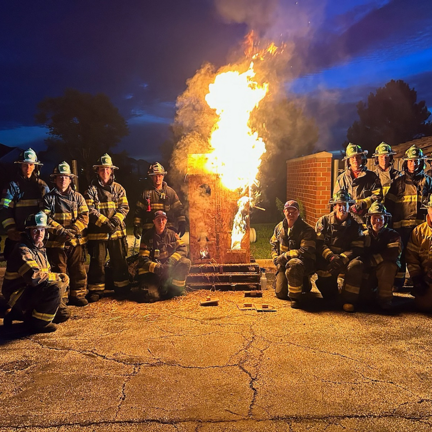 Firefighters posed around a large controlled blaze at night on an asphalt street