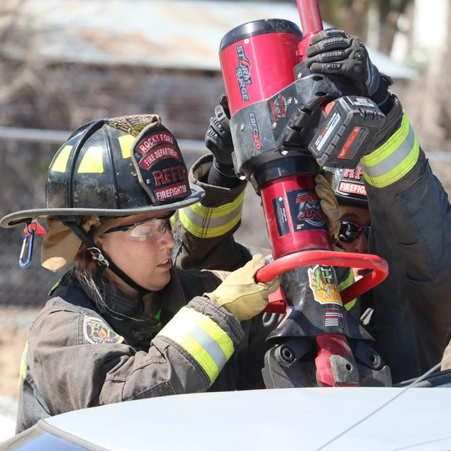 Firefighters in helmets handling a red rescue tool at an accident scene