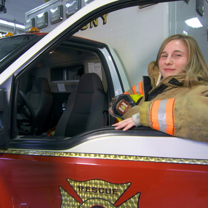 Firefighter seated in a red rescue vehicle, smiling and holding a radio beside the open door