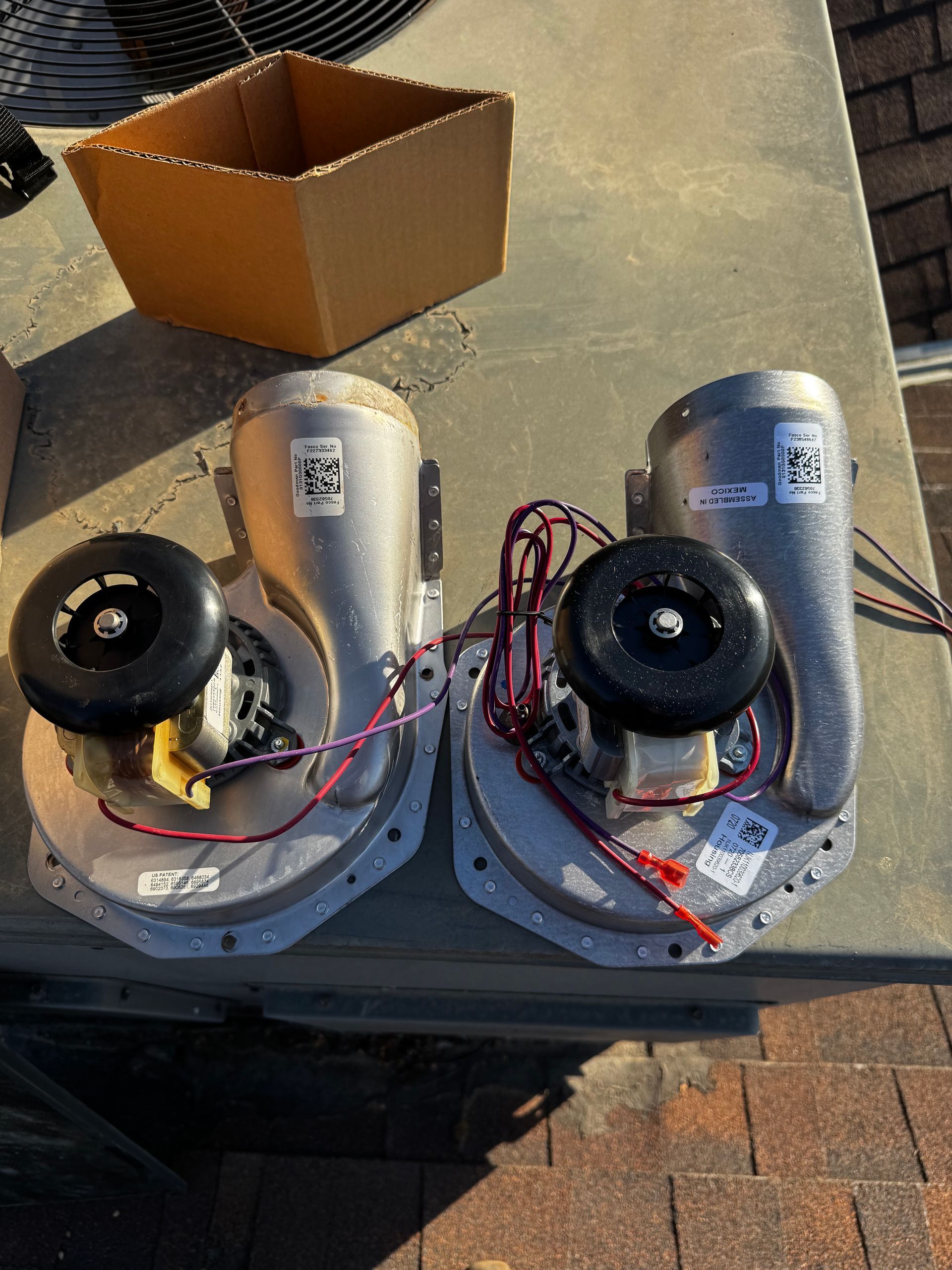 Two fans are sitting on a table next to a cardboard box.