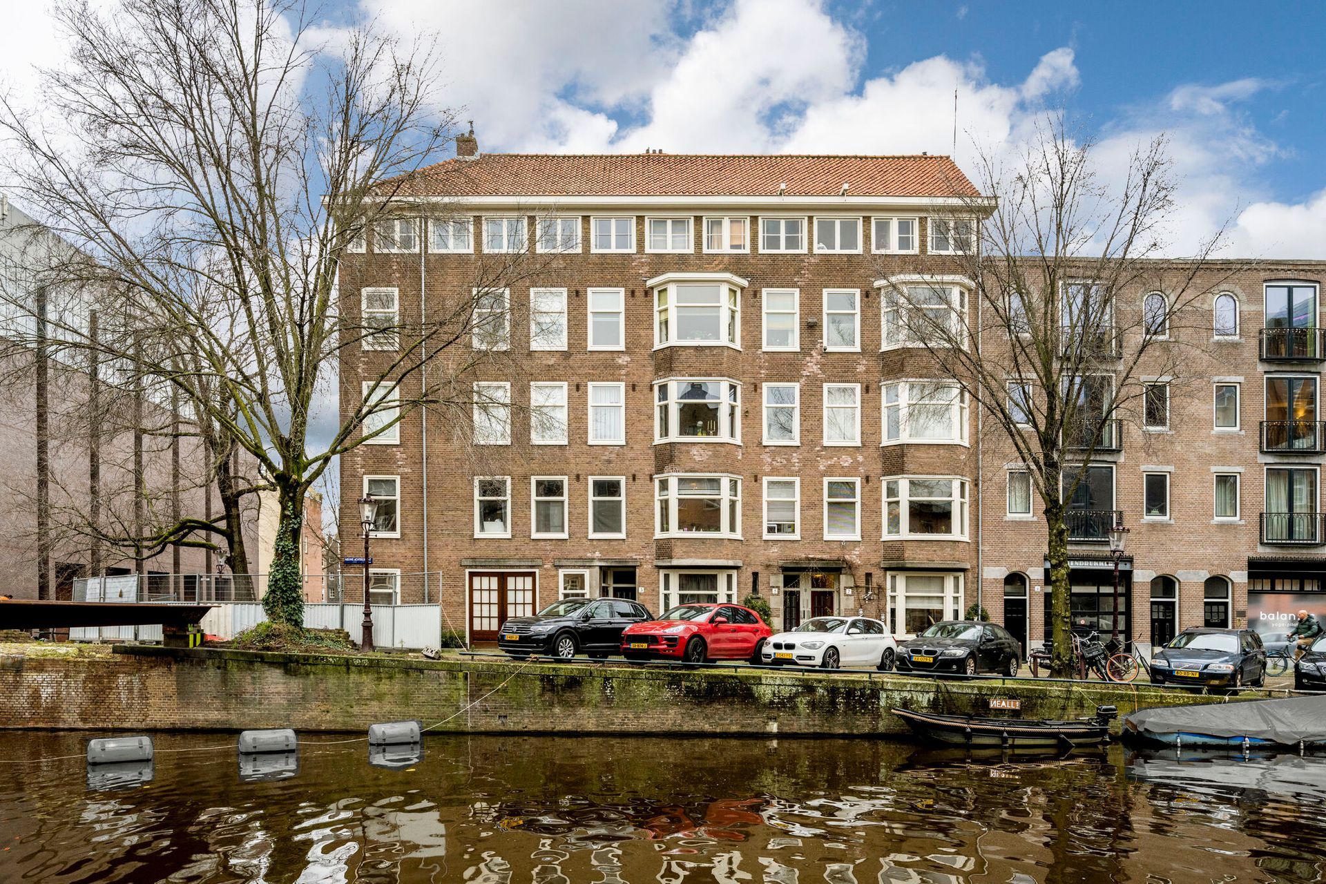 Een groot gebouw met ervoor geparkeerde auto's, naast een rivier.