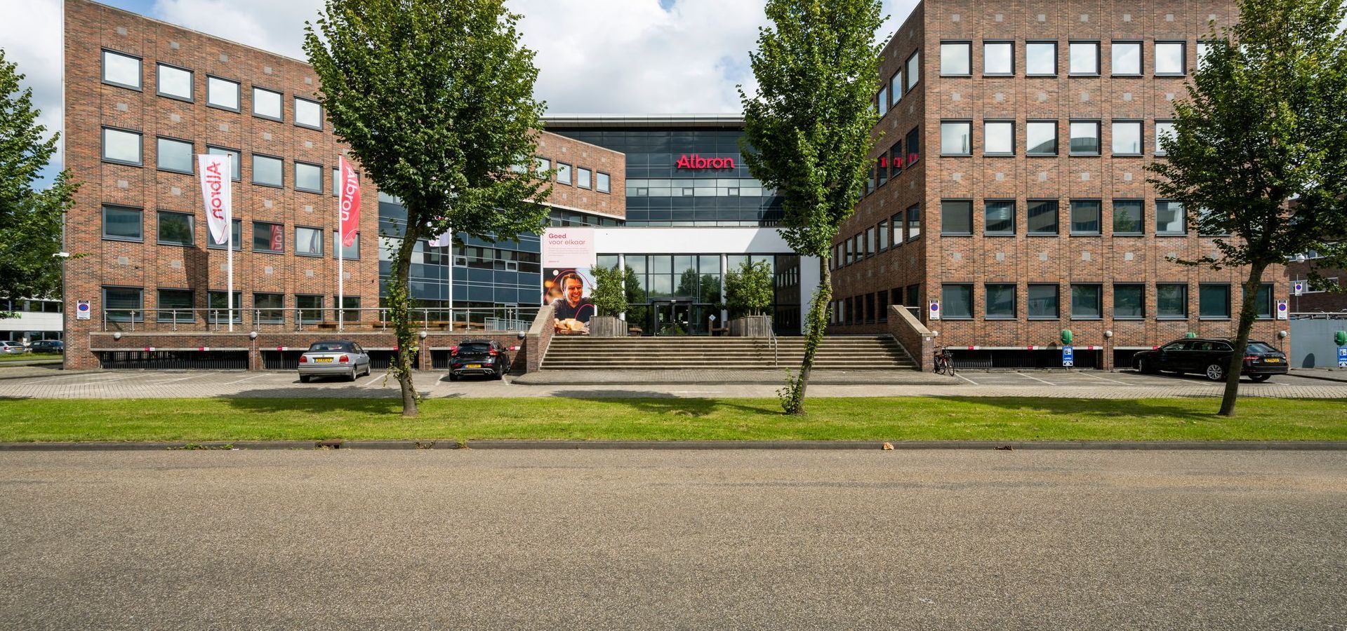 Een groot bakstenen gebouw met veel ramen staat aan de kant van de weg.