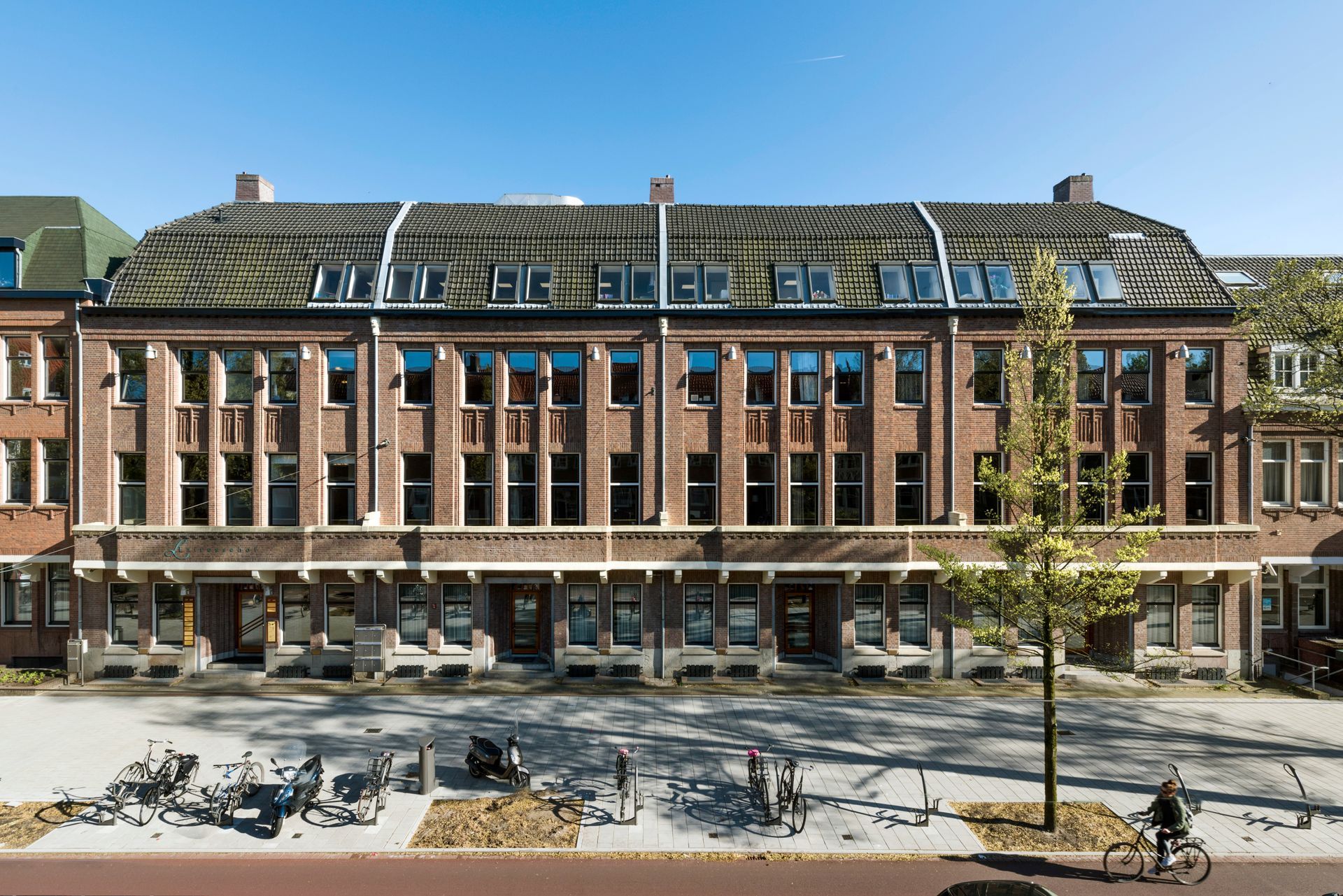 Een groot bakstenen gebouw met veel ramen en een boom ervoor