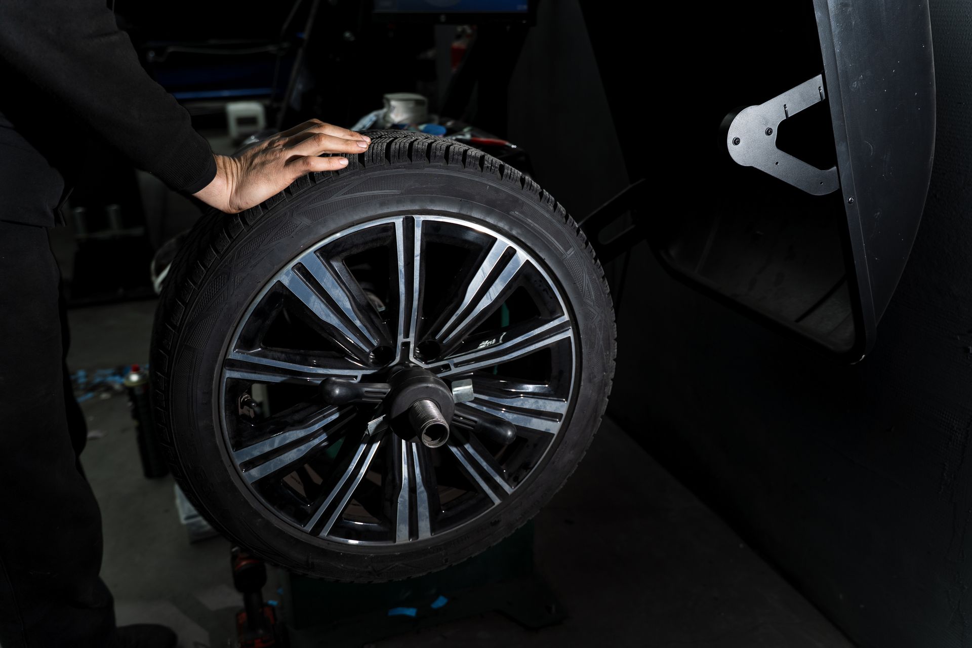 Hand touching a car wheel with a black alloy rim in a dark garage