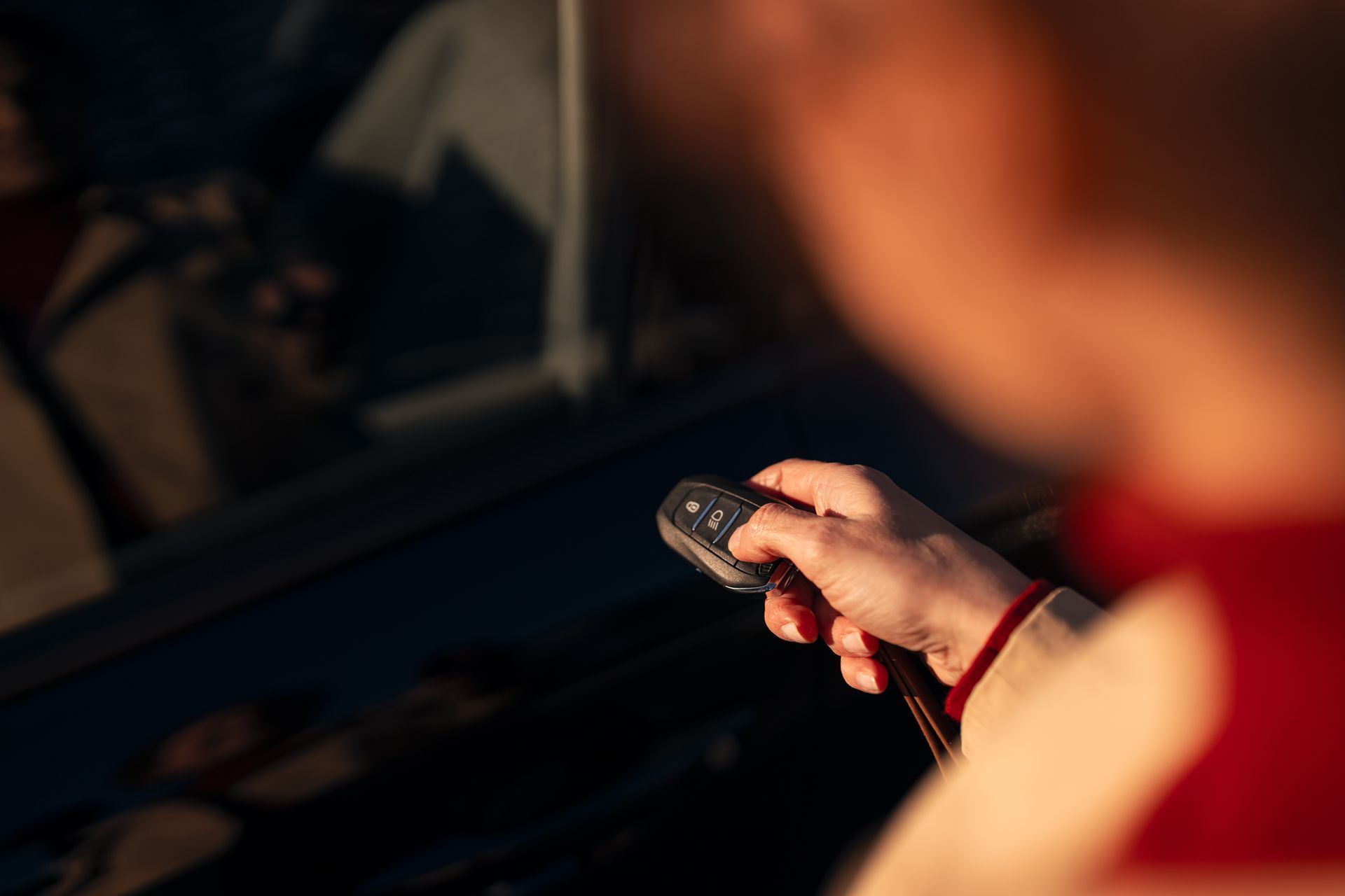 Person holding a car key fob near a vehicle door at dusk