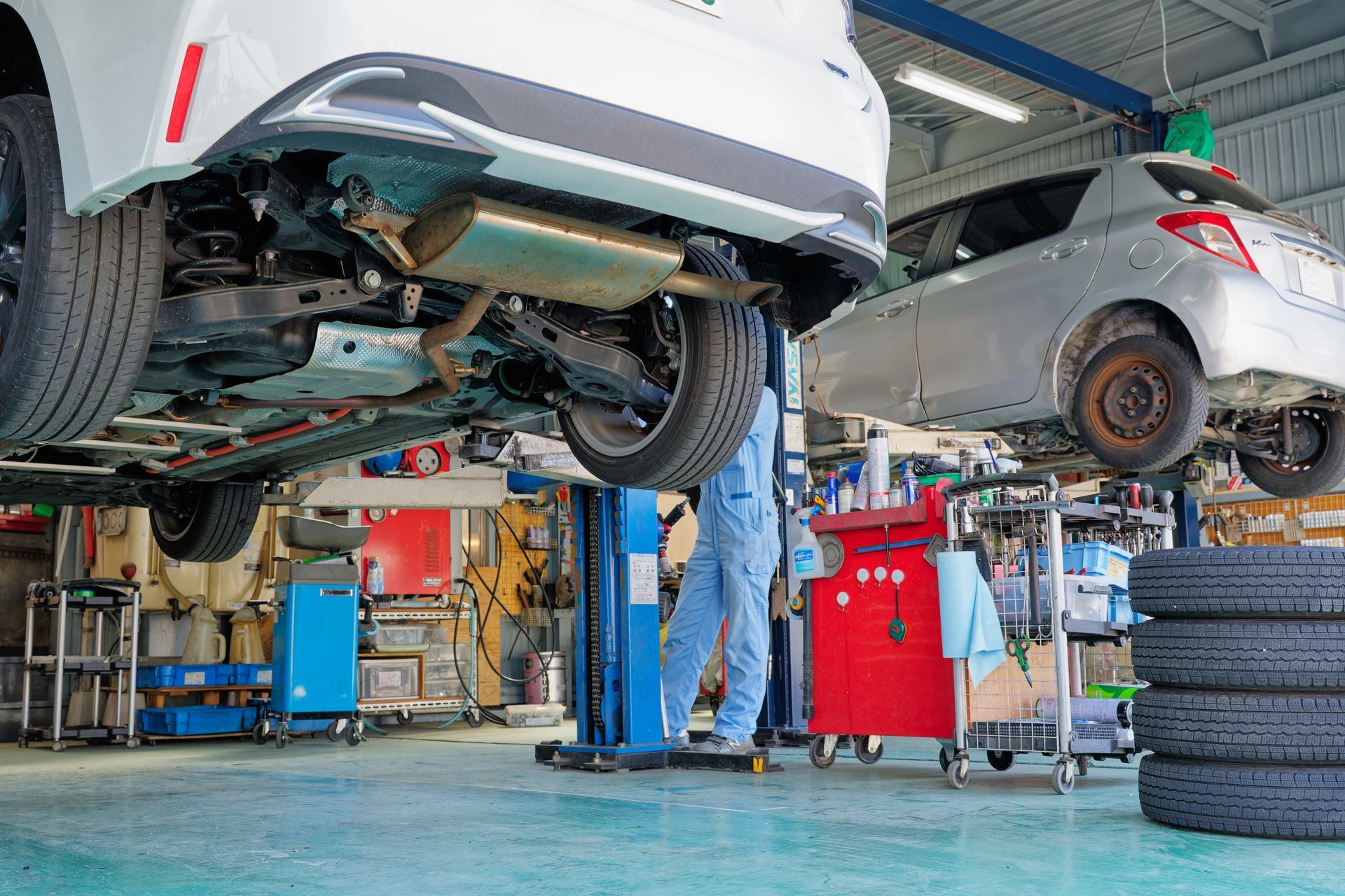 Cars lifted on a repair shop hoist with a mechanic underneath and tools nearby Cars lifted on a repair shop hoist with a mechanic underneath and tools nearby