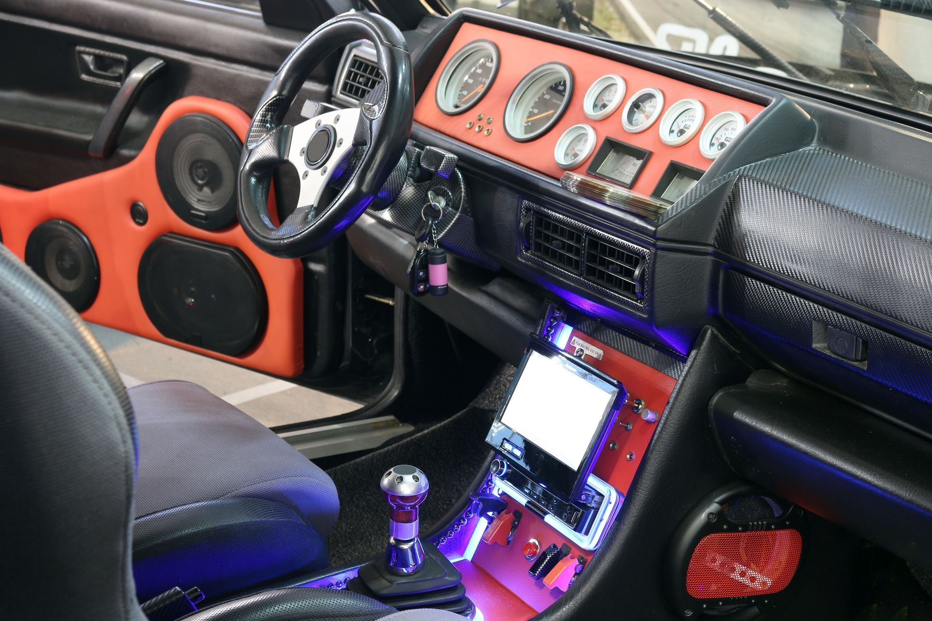 Custom car interior with orange accents, gauges on dashboard, steering wheel, and illuminated center console
