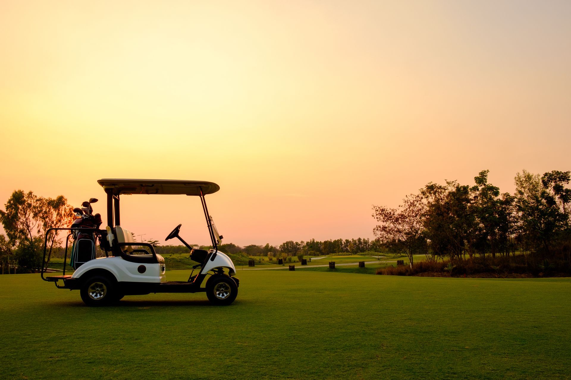 Golf cart on a green course at sunset, silhouetted against an orange sky.