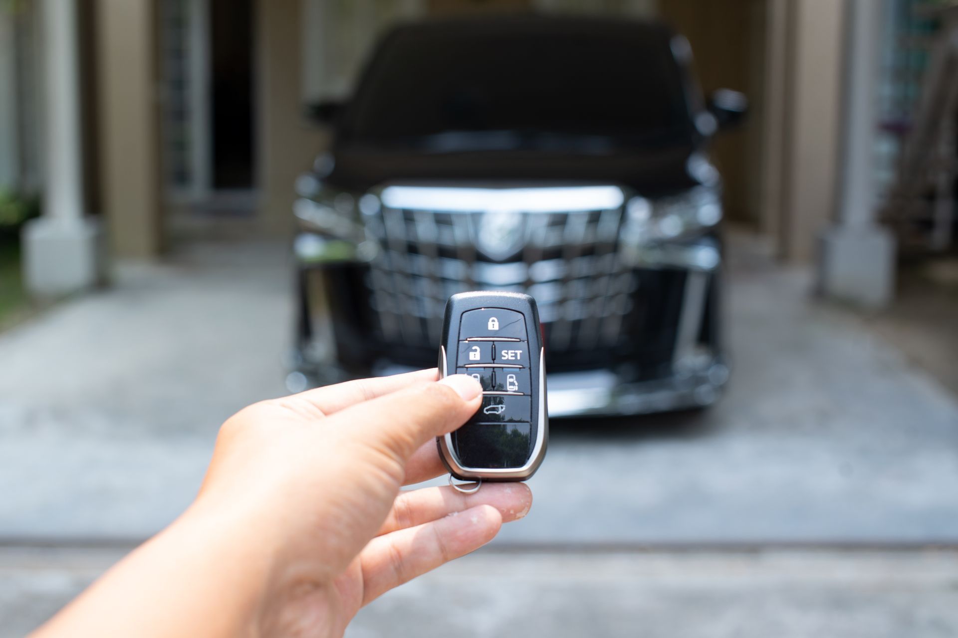 Hand holding a car key fob toward a black SUV parked in a driveway