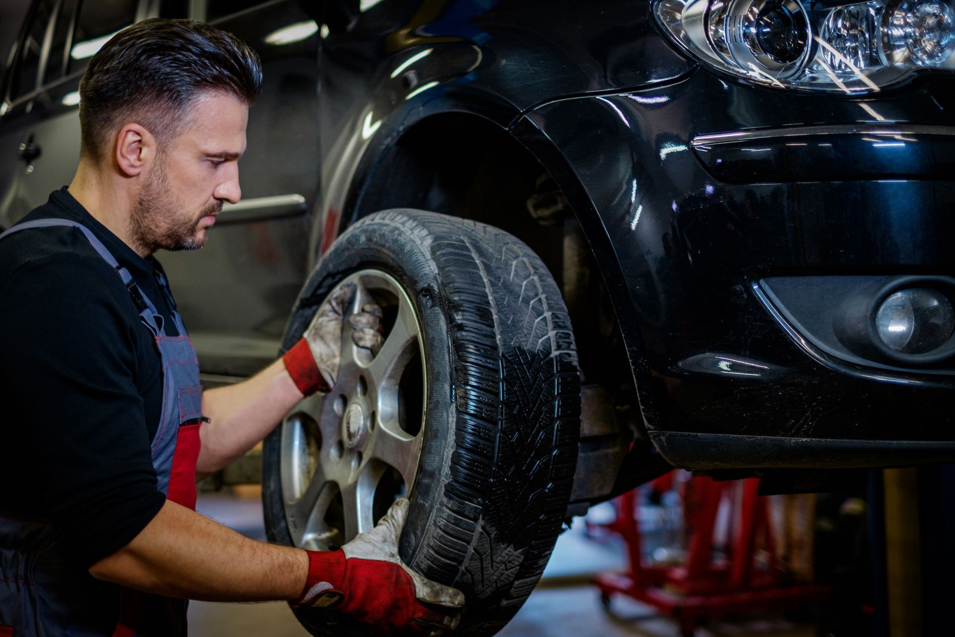Mechanic in red gloves removing a car wheel in an auto repair shop