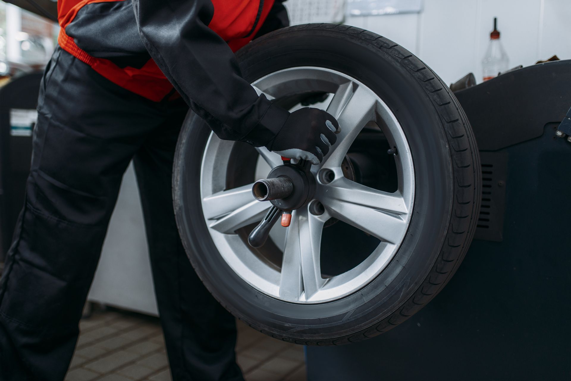Mechanic holding a car wheel in a garage, with a silver alloy rim and black tire