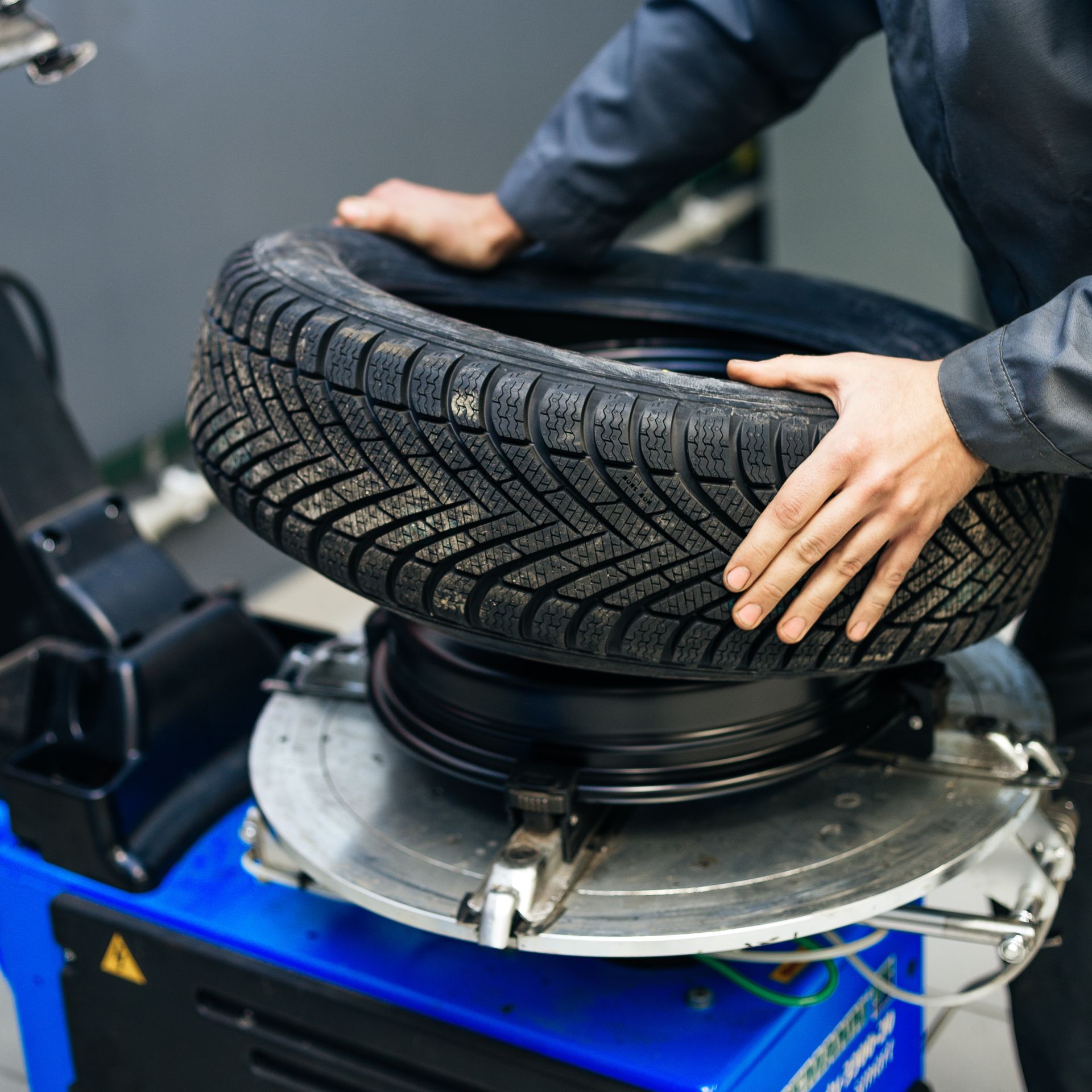 Hands mounting a car tire onto a blue tire-changing machine in a workshop