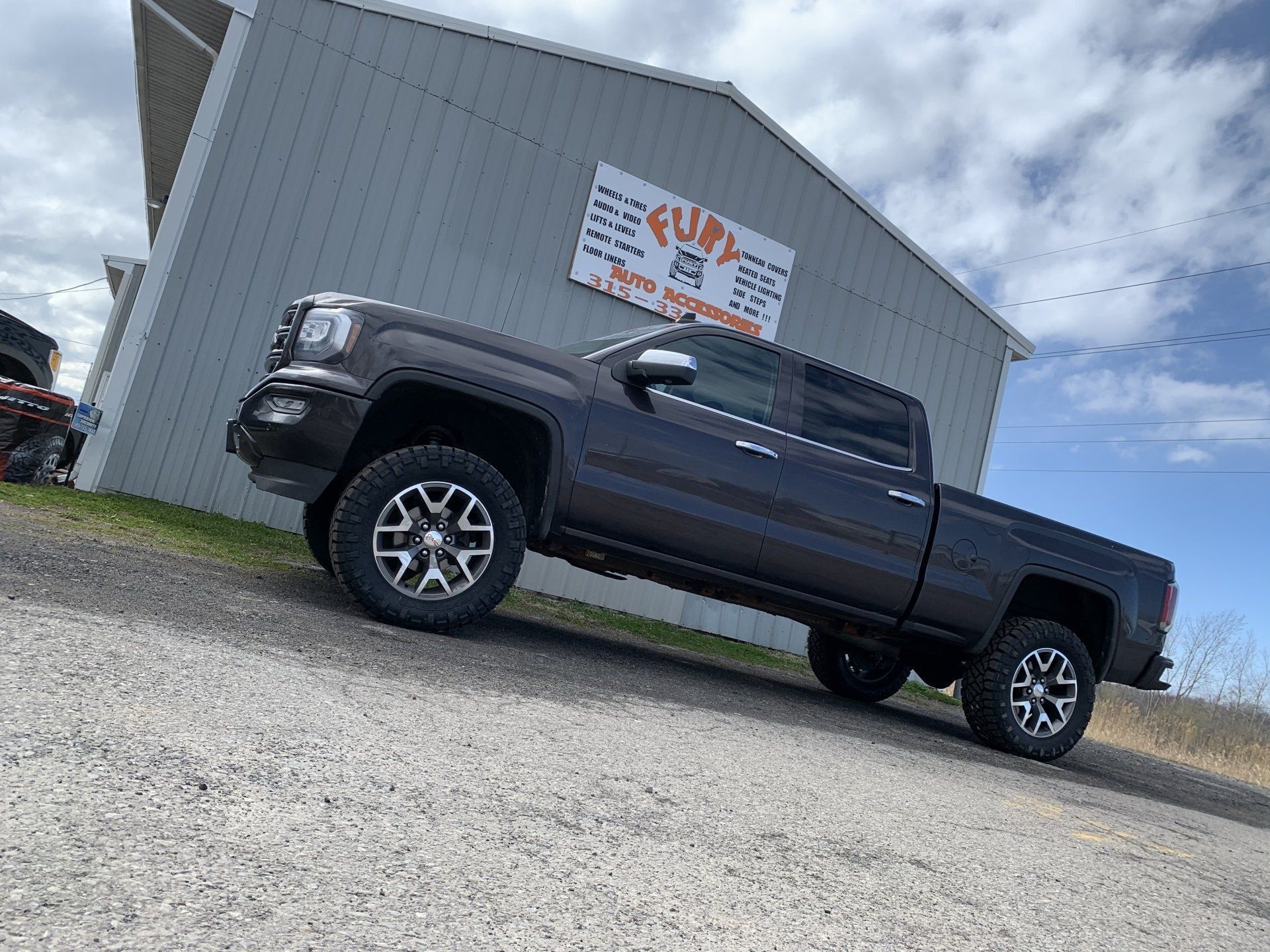 Dark pickup truck parked beside a gray industrial building under a cloudy sky.