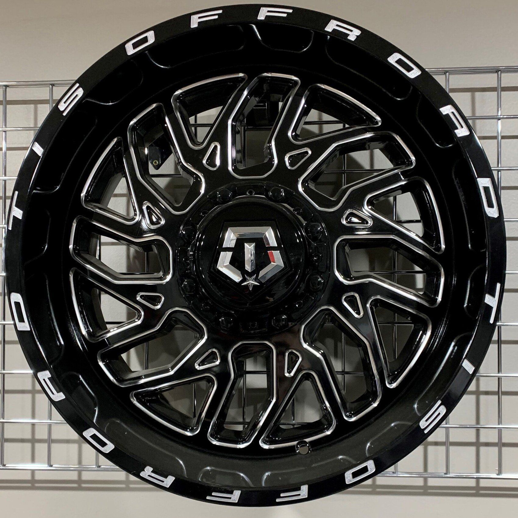Black off-road wheel rim with silver accents and bold white lettering, centered against a plain background