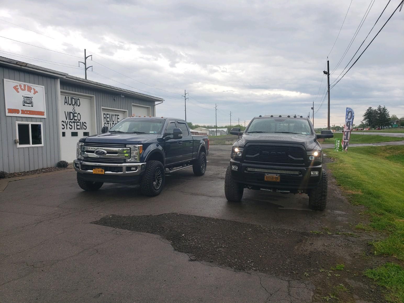 Two black pickup trucks parked on a wet roadside under cloudy skies