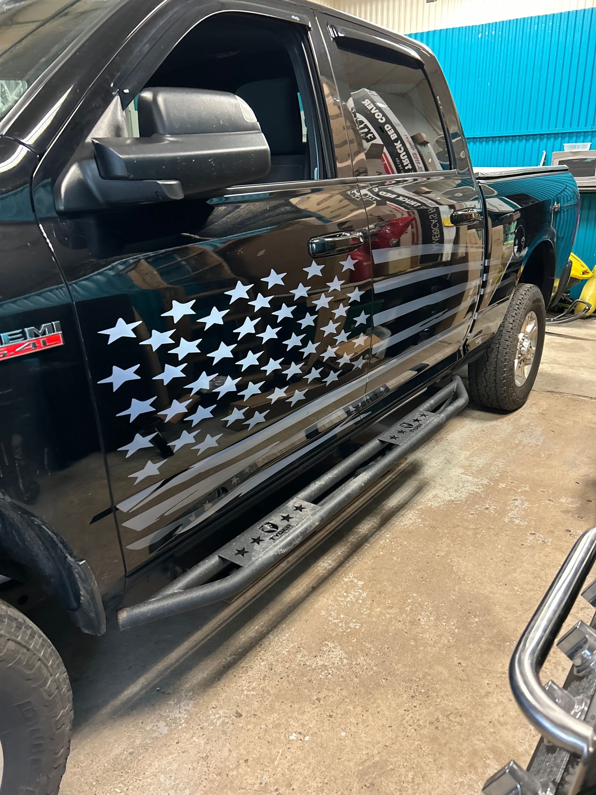 Black pickup truck with American flag stars-and-stripes decal, parked indoors on a workshop floor.
