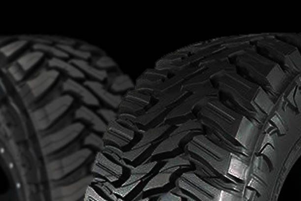 Close-up of two rugged black off-road tires with deep tread patterns against a dark background