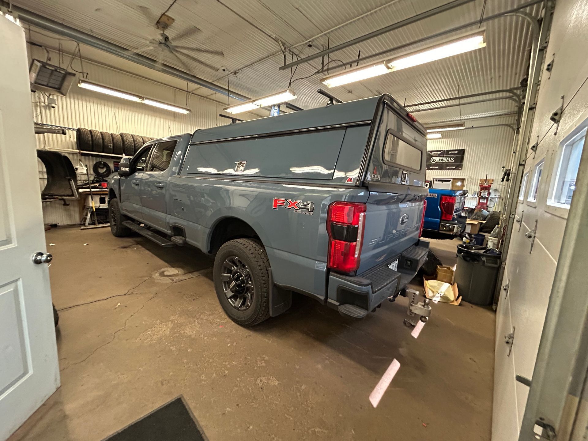 Gray pickup truck in an auto shop garage, viewed from the rear side.