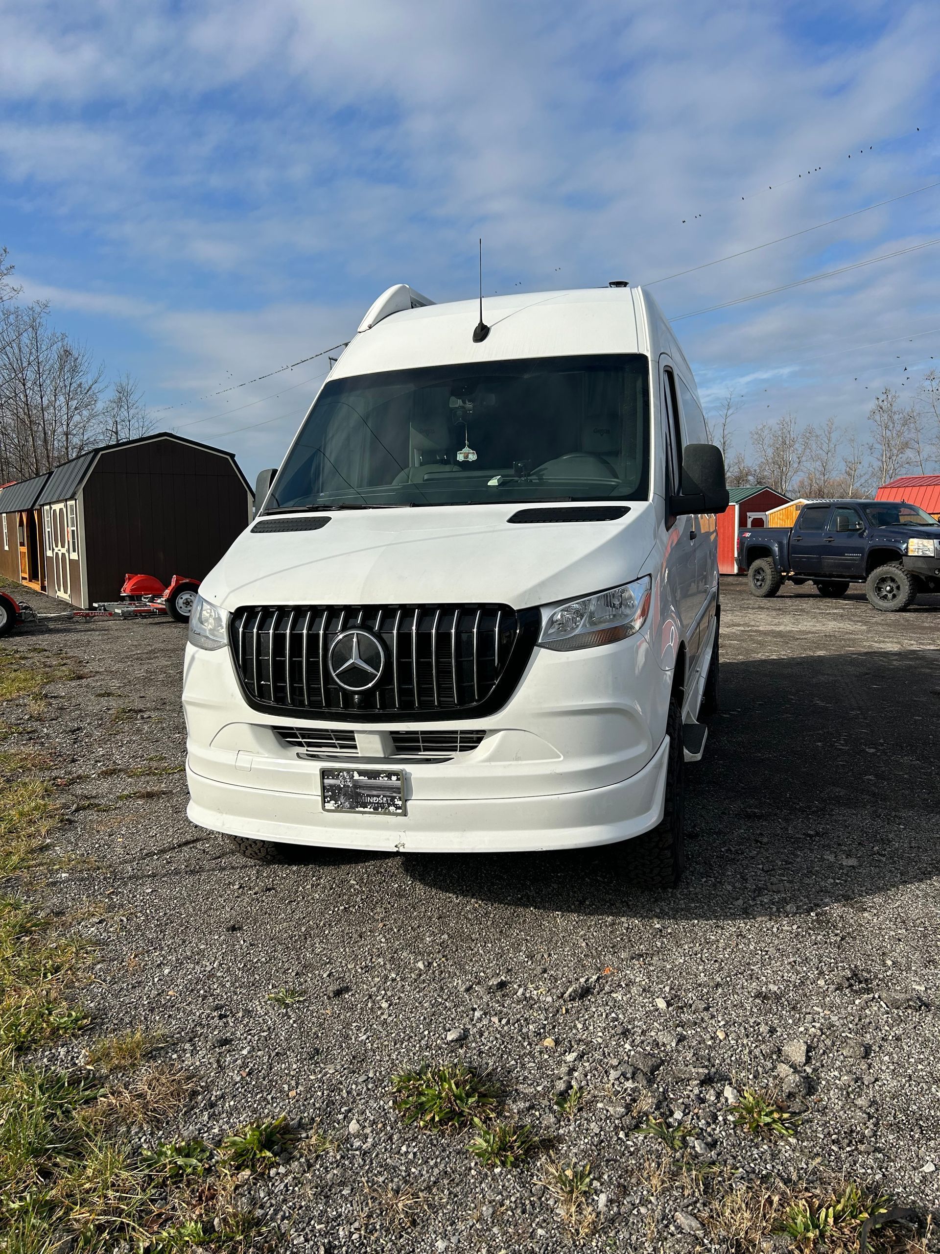 White Mercedes van parked on gravel lot under a partly cloudy sky.
