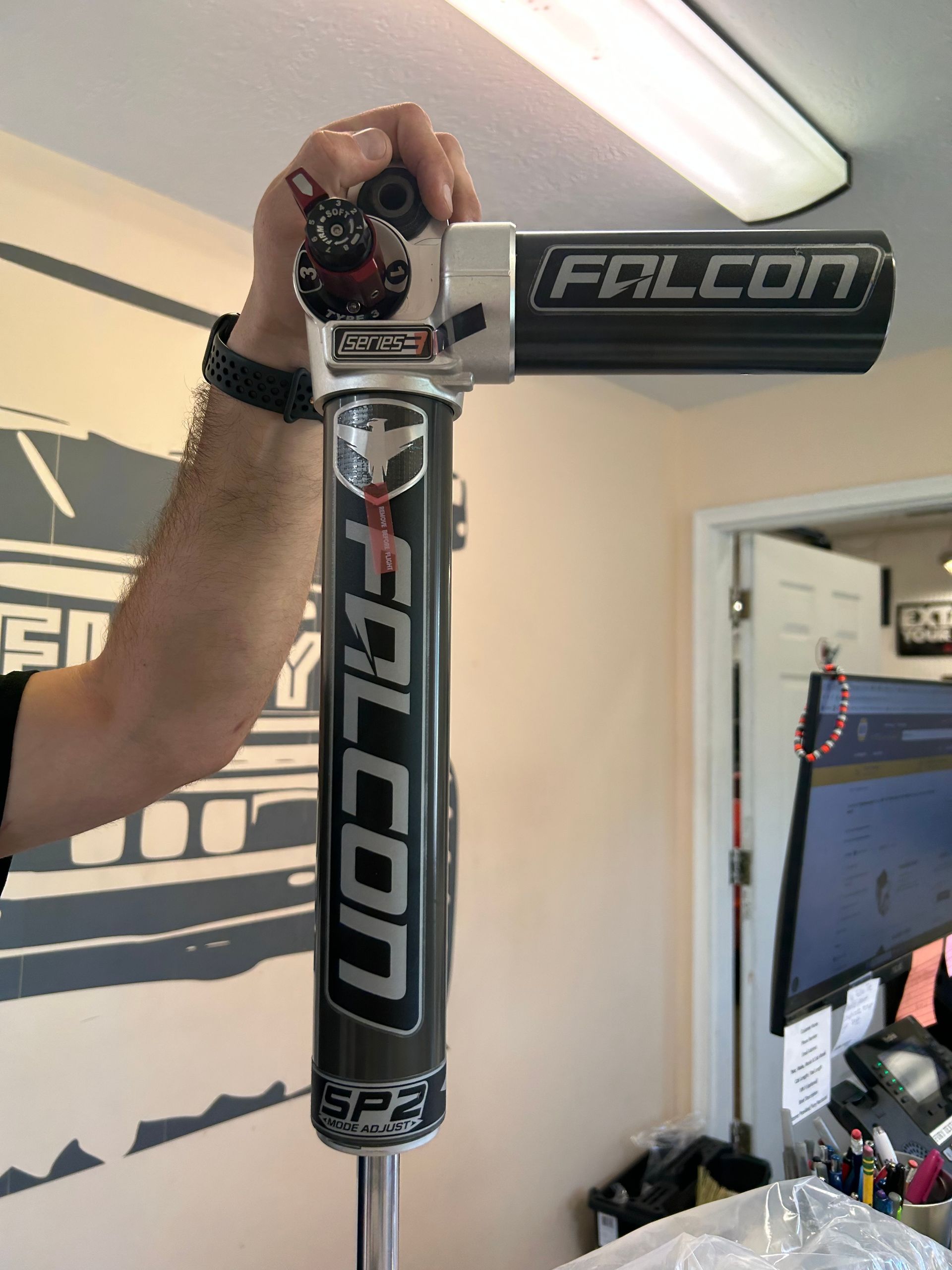 Person holding a black and gray Falcon mountain bike frame indoors