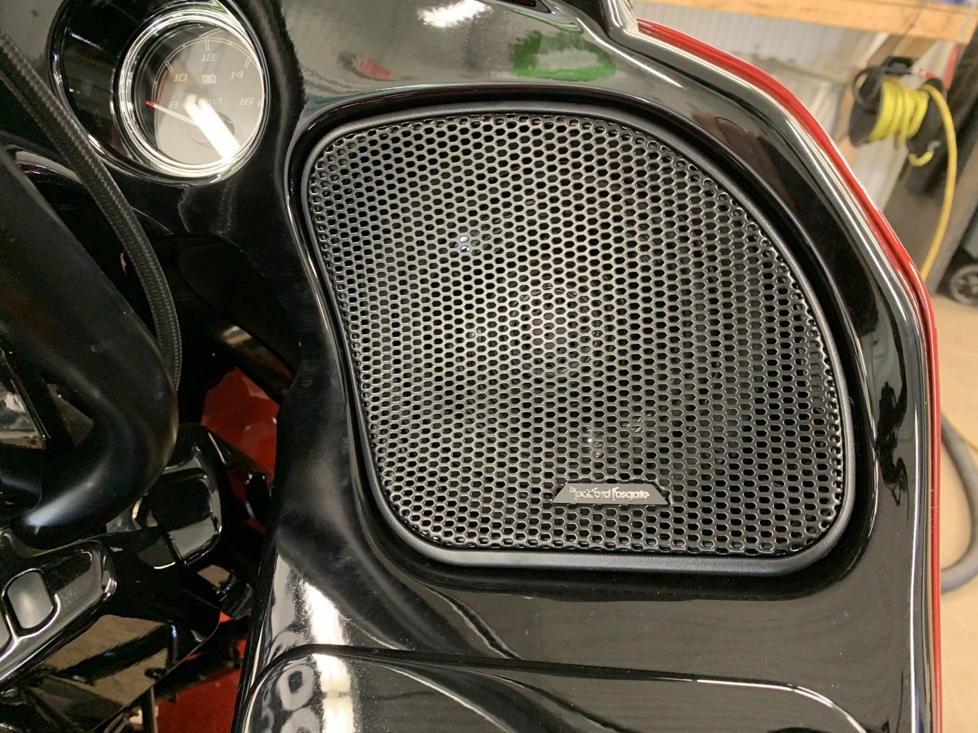 Close-up of a black car door speaker grille with a small badge and chrome trim