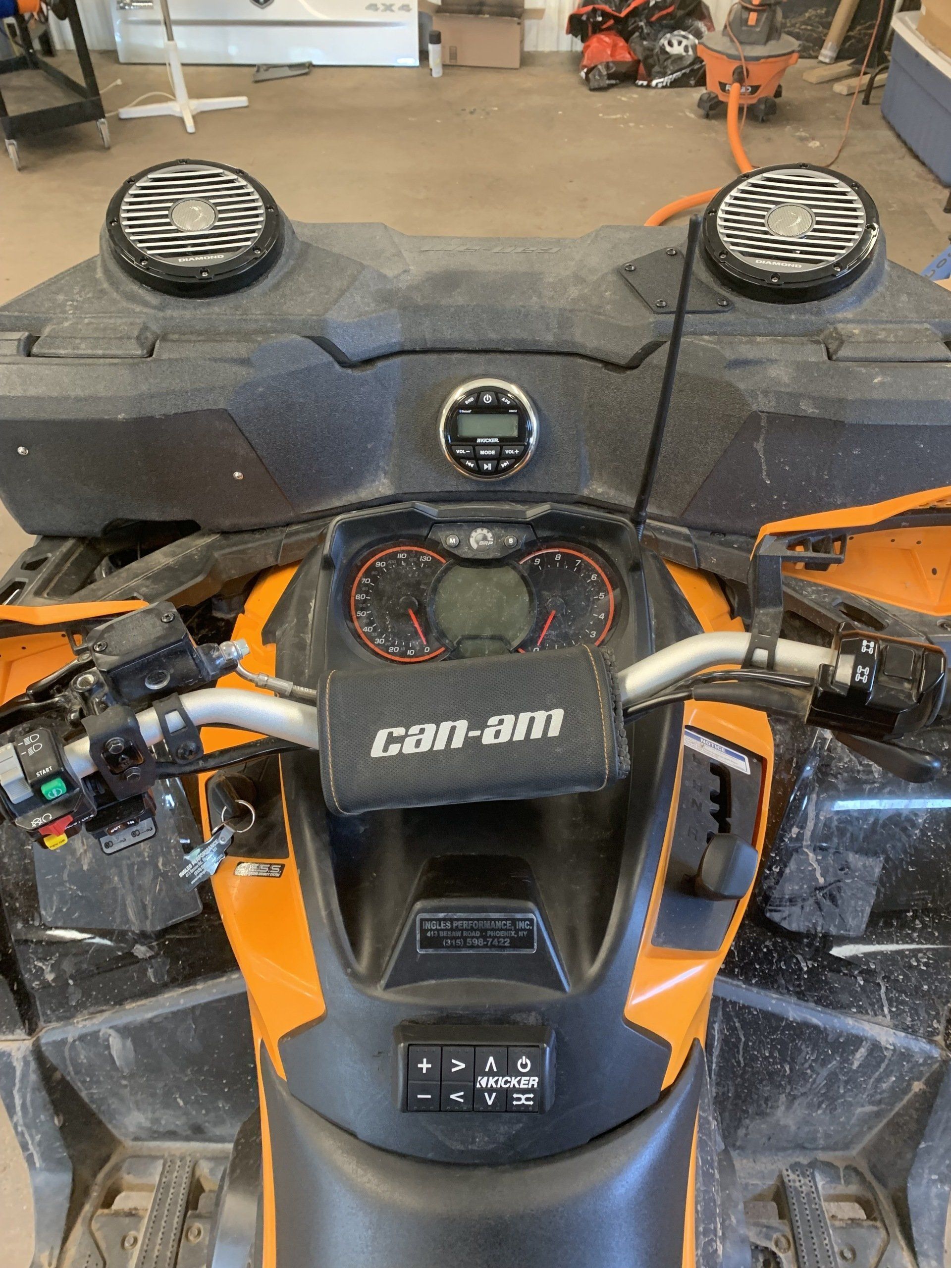 POV from an ATV seat, showing black-and-orange controls and speaker pods on the handlebars and front rack.