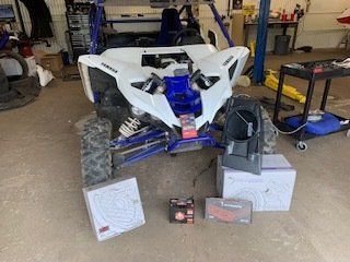 White and blue ATV in a garage, with parts and boxes on the floor nearby.