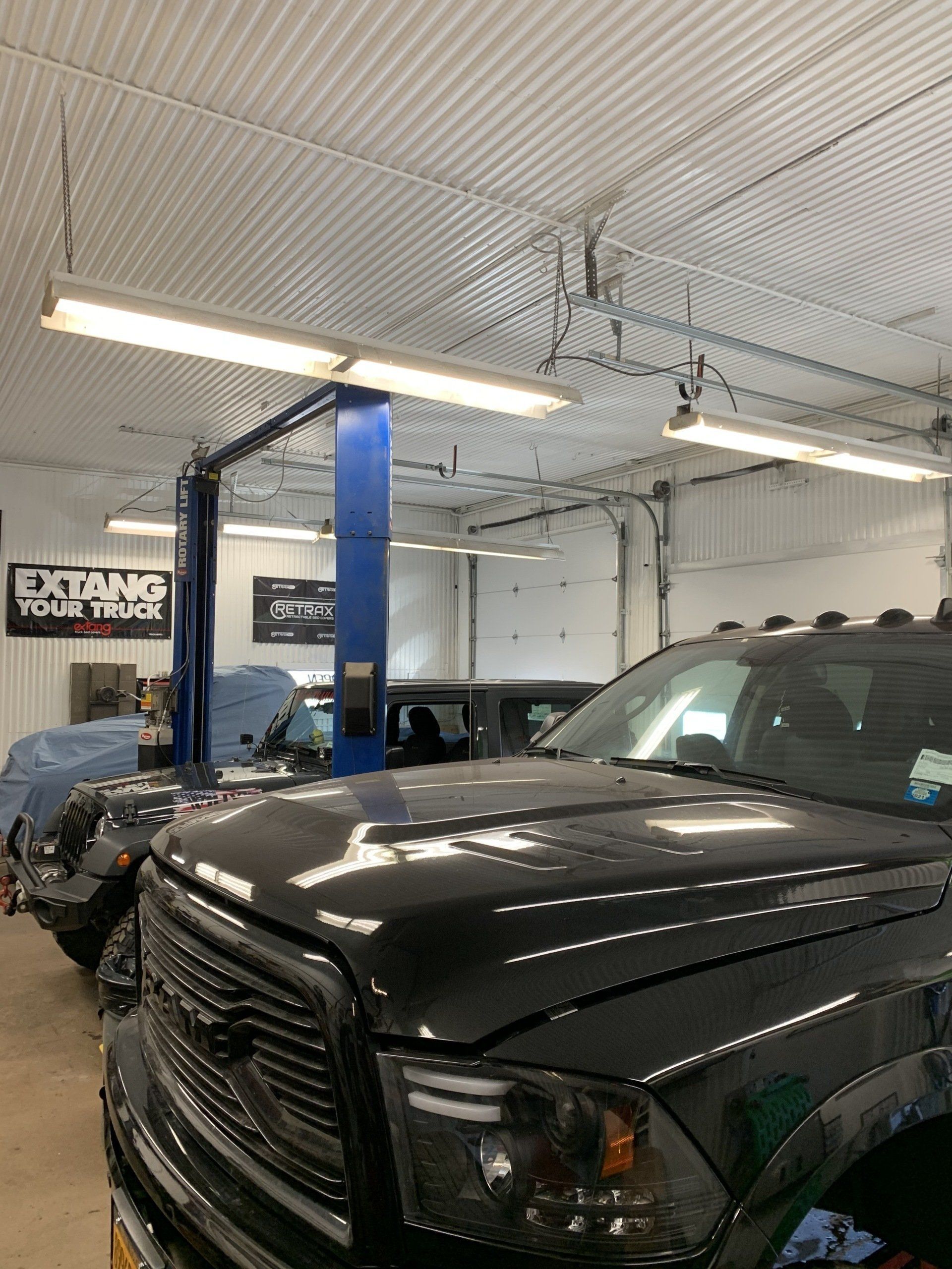 Black pickup truck in an auto repair shop under bright fluorescent lights
