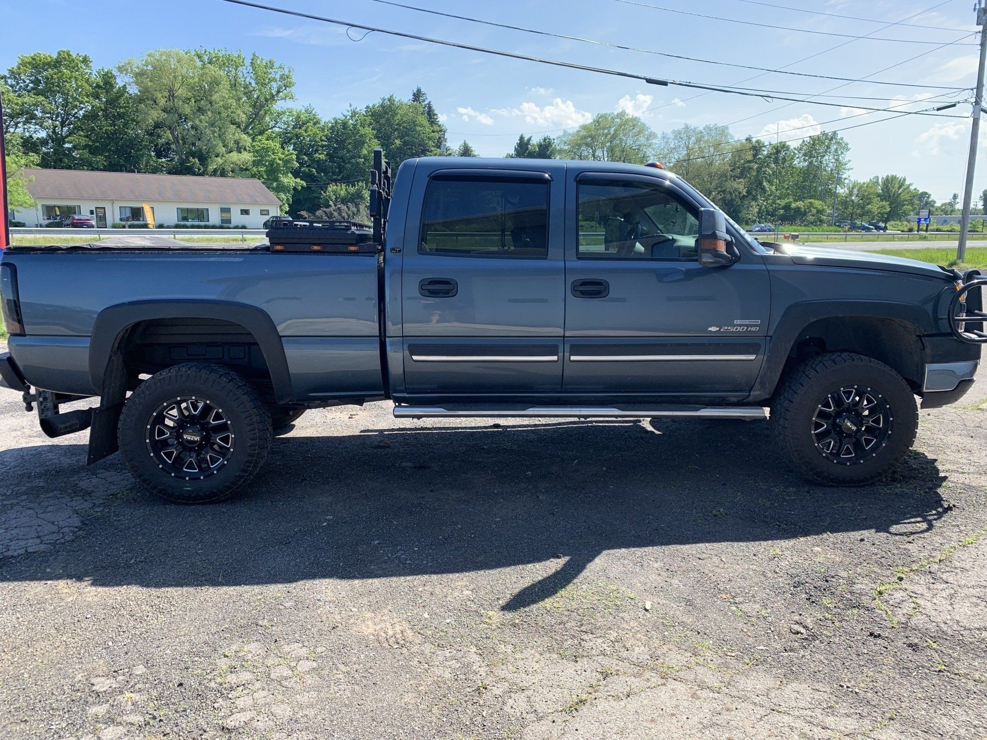 Dark gray crew cab pickup truck parked on gravel under a sunny sky