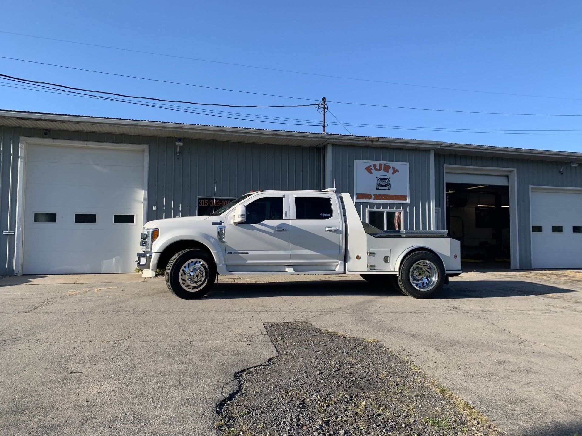 White tow truck parked outside an auto shop with two garage bays under a clear blue sky