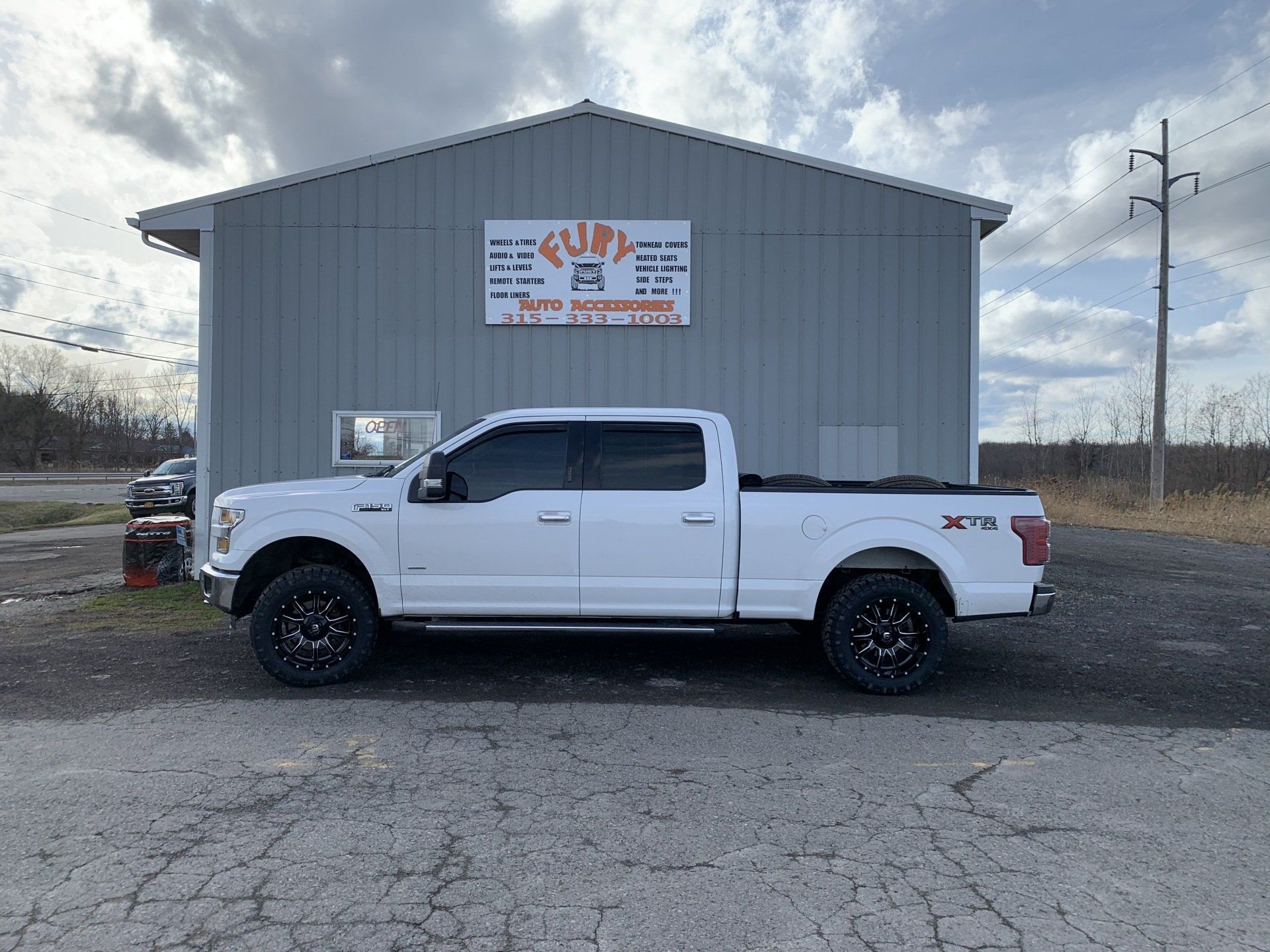 White GMC pickup truck parked in front of a gray shop building with a sign.