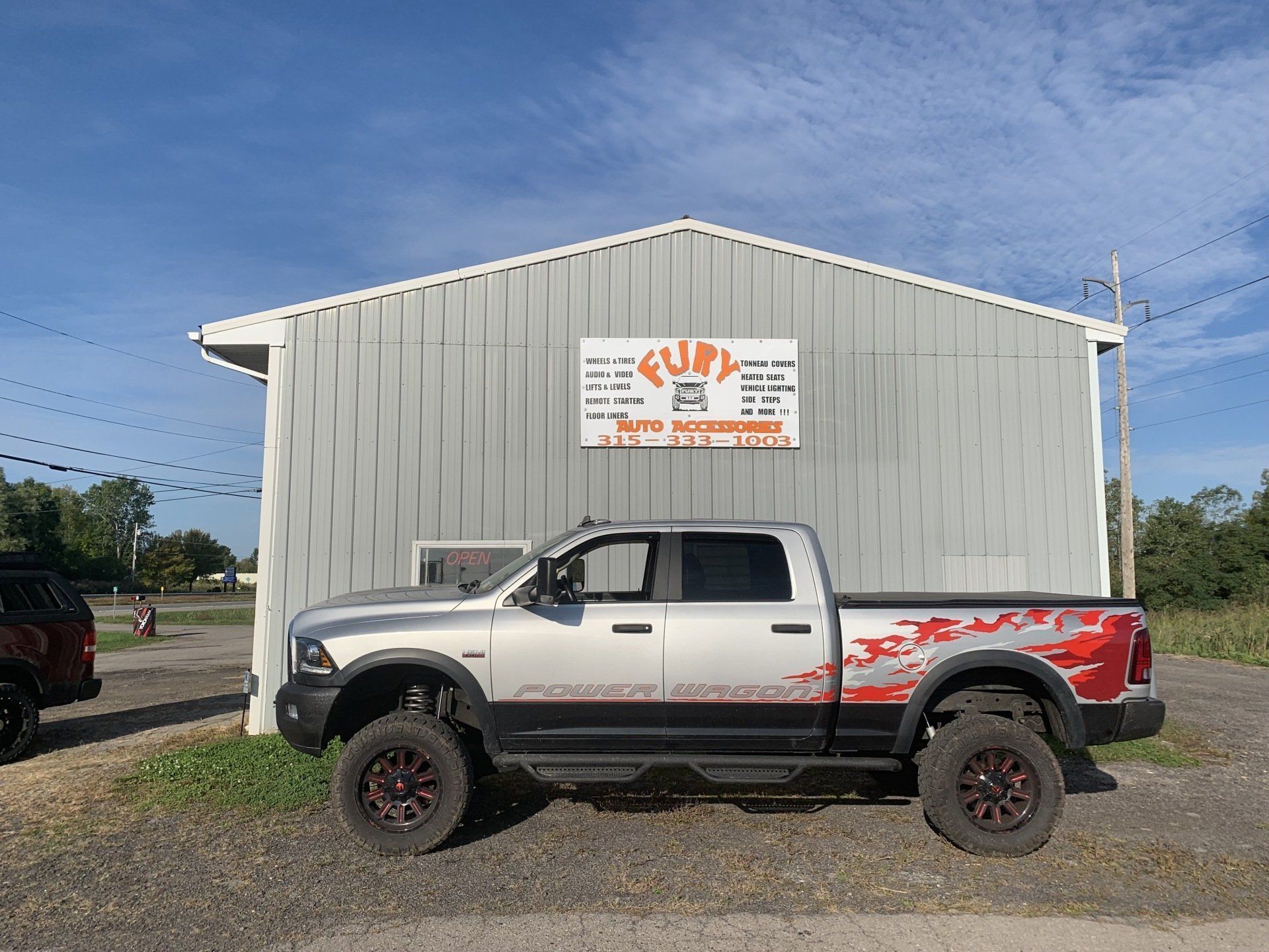 White lifted pickup truck parked in front of a gray metal building with an orange sign.
