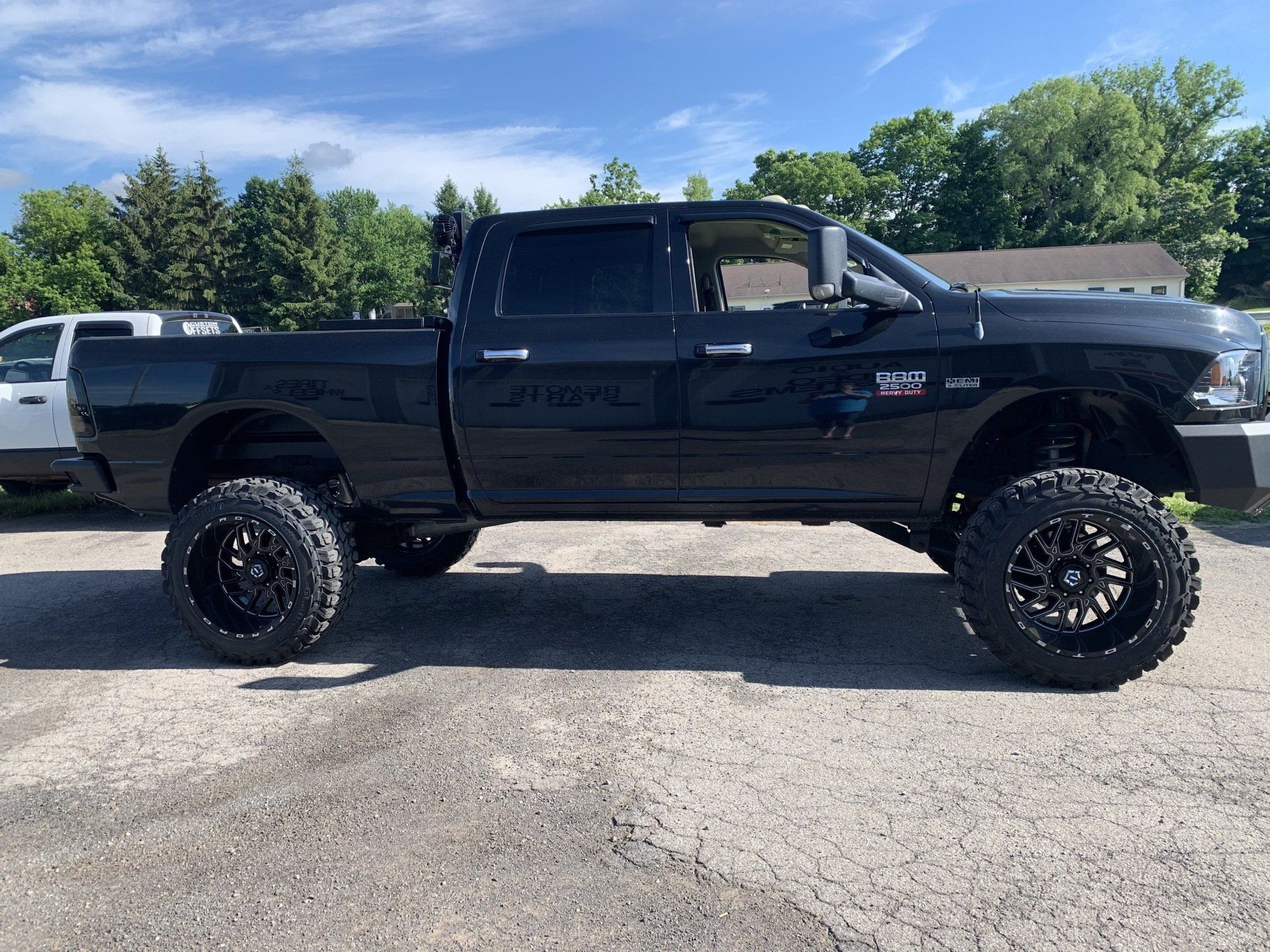 Black lifted pickup truck parked on gravel lot under a blue sky