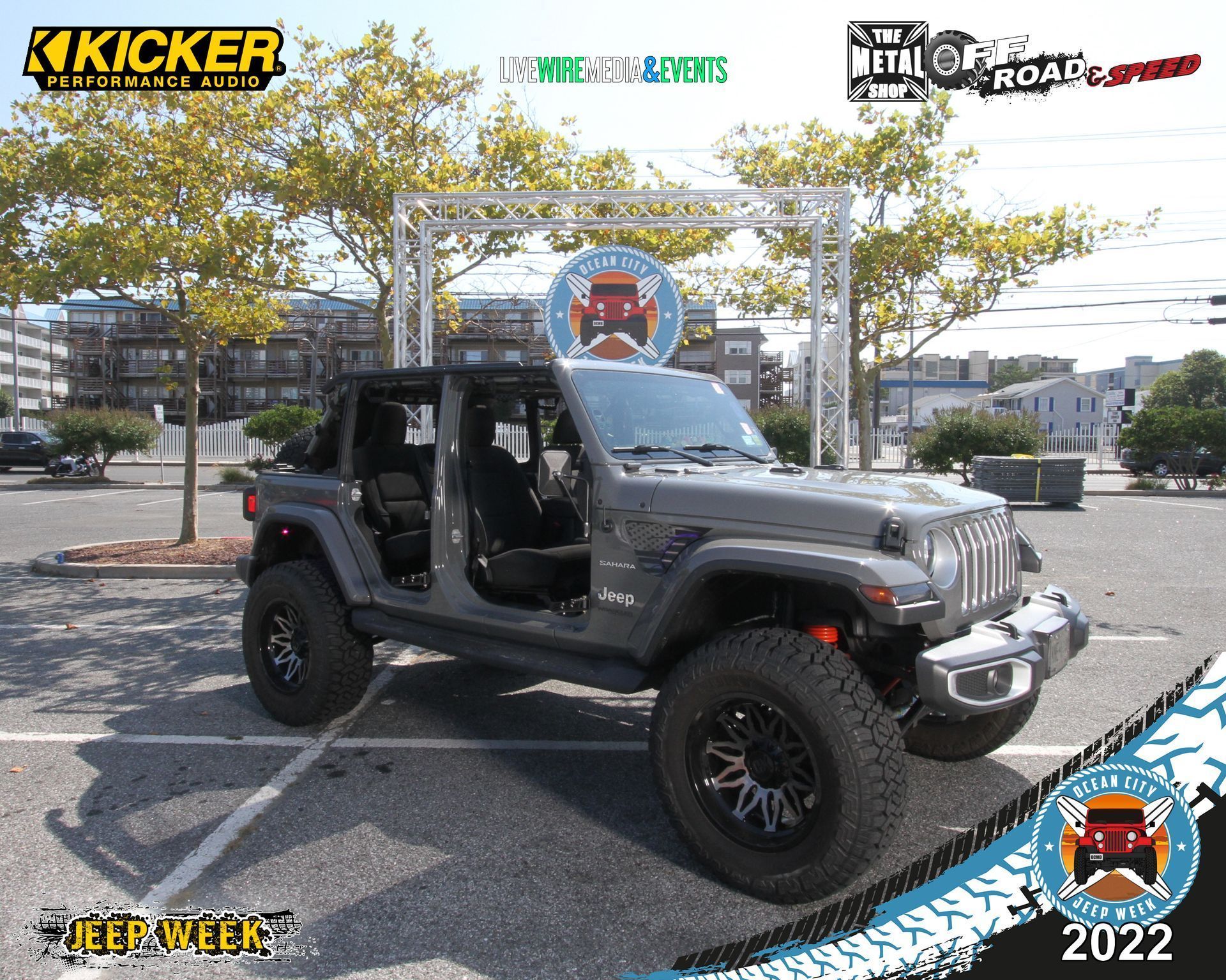 Lifted black Jeep Wrangler with doors off parked outdoors at a car event, with sponsor logos and “2022” overlay