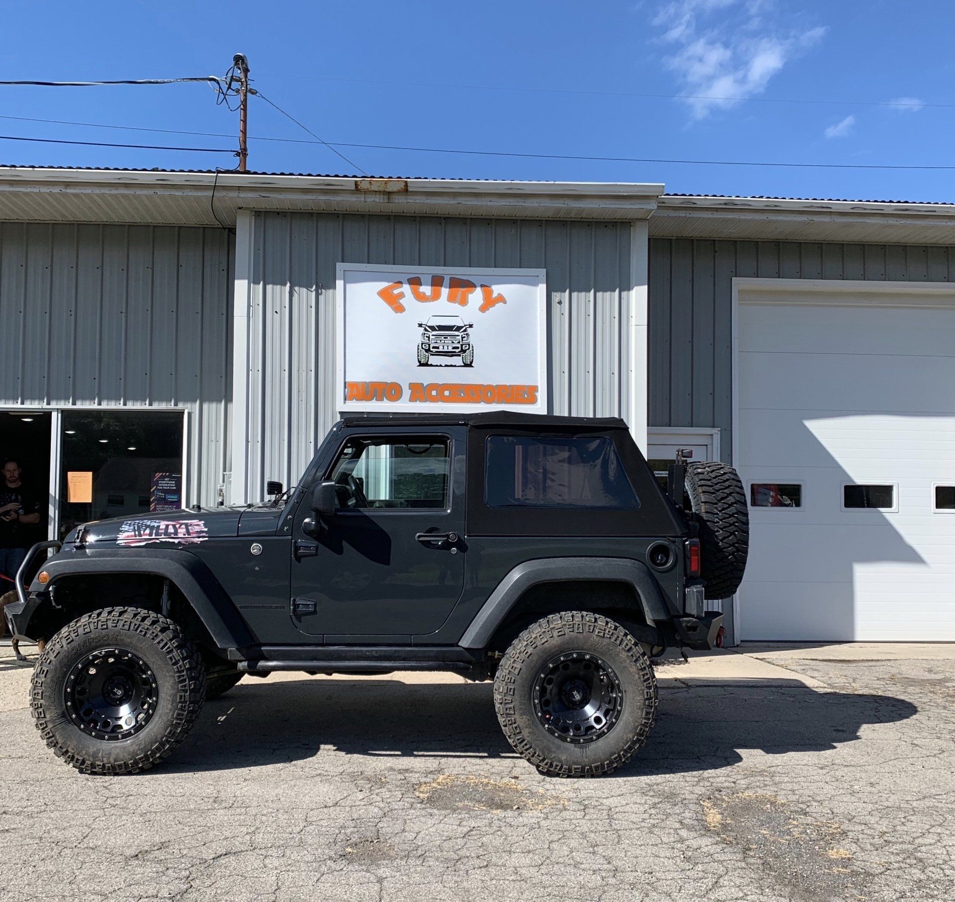 Black off-road Jeep parked outside a garage with a FUEL sign on a sunny day