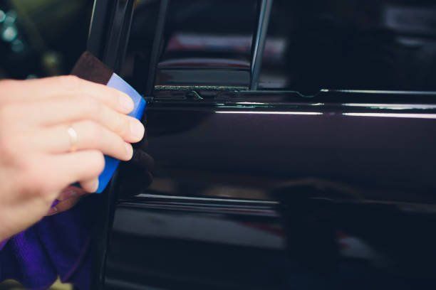 Hand using a blue cloth to wipe a black car door handle