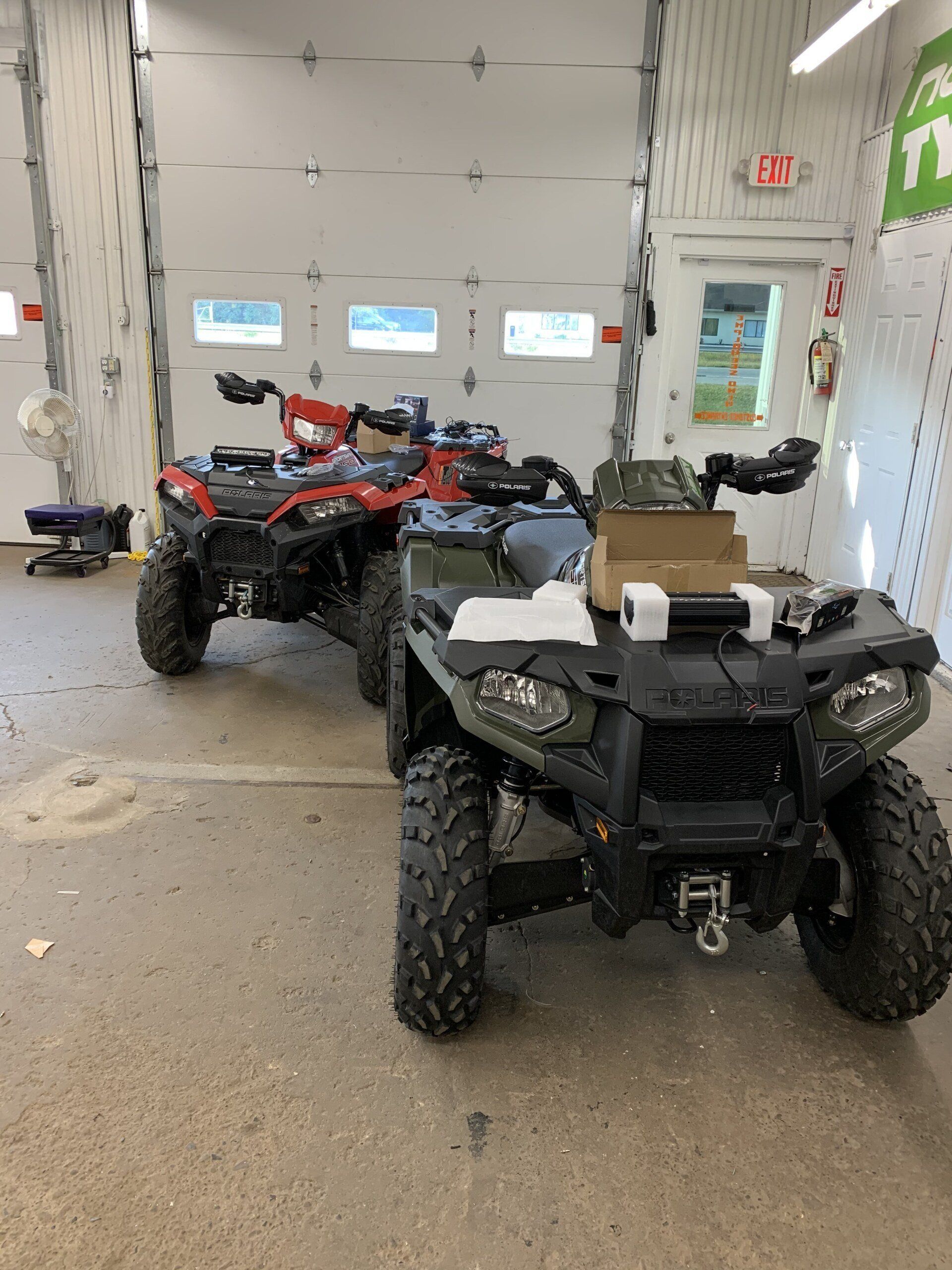 ATVs parked inside a garage, with a black ATV in the foreground and a red one behind it.