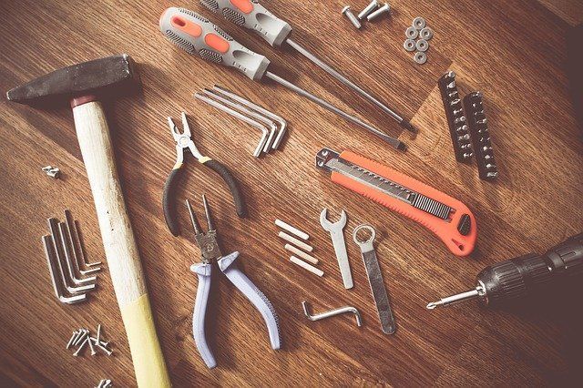 A wooden table topped with a hammer , pliers , screwdrivers , wrenches and other tools.