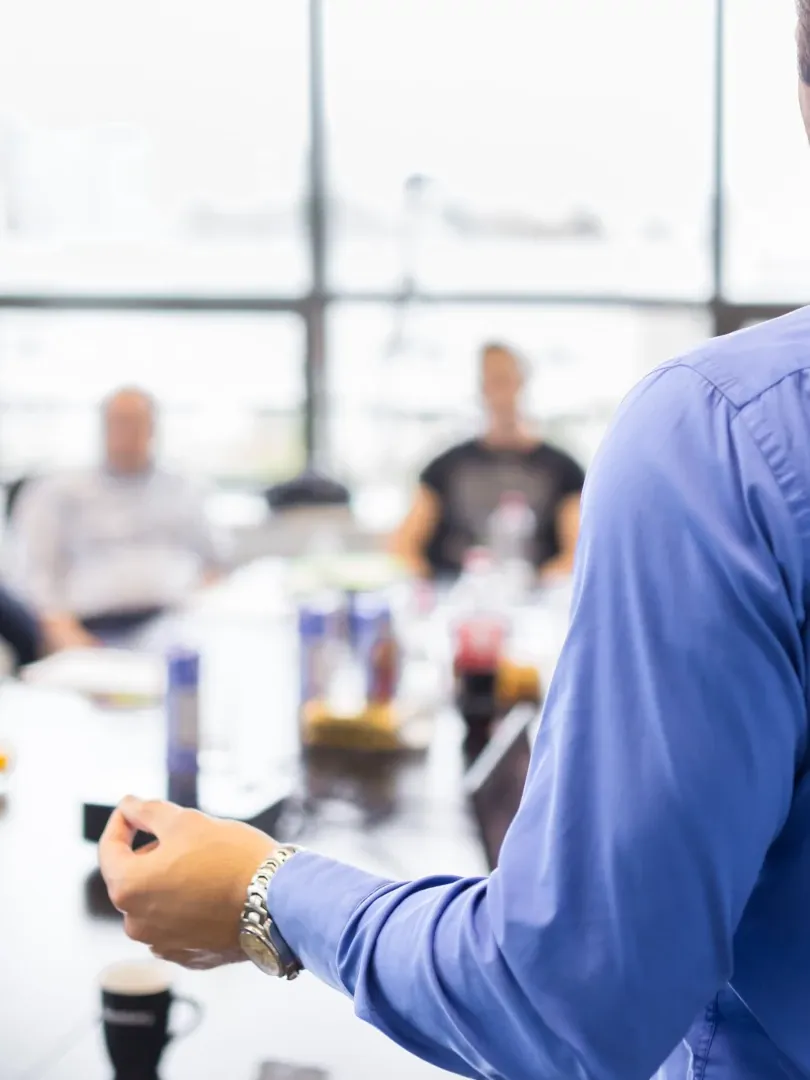 Presenter gesturing in a bright conference room with blurred attendees in the background