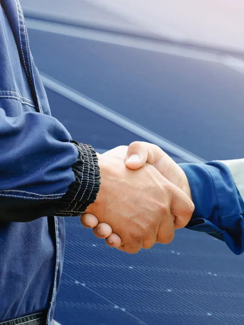 Two people in blue jackets shaking hands outdoors near a car