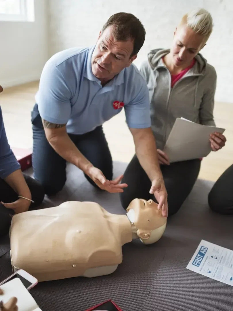 Two people demonstrate CPR on a training manikin in a classroom setting