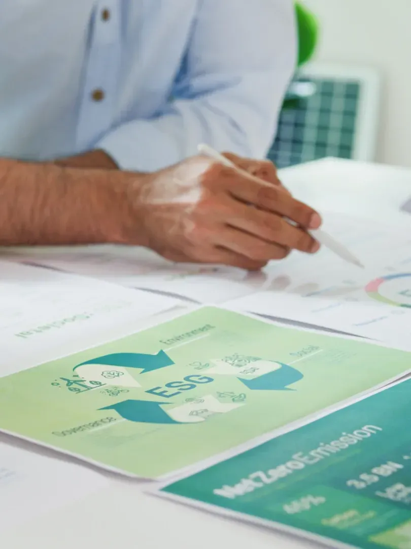 Hand holding a pen over printed documents with green charts on a desk