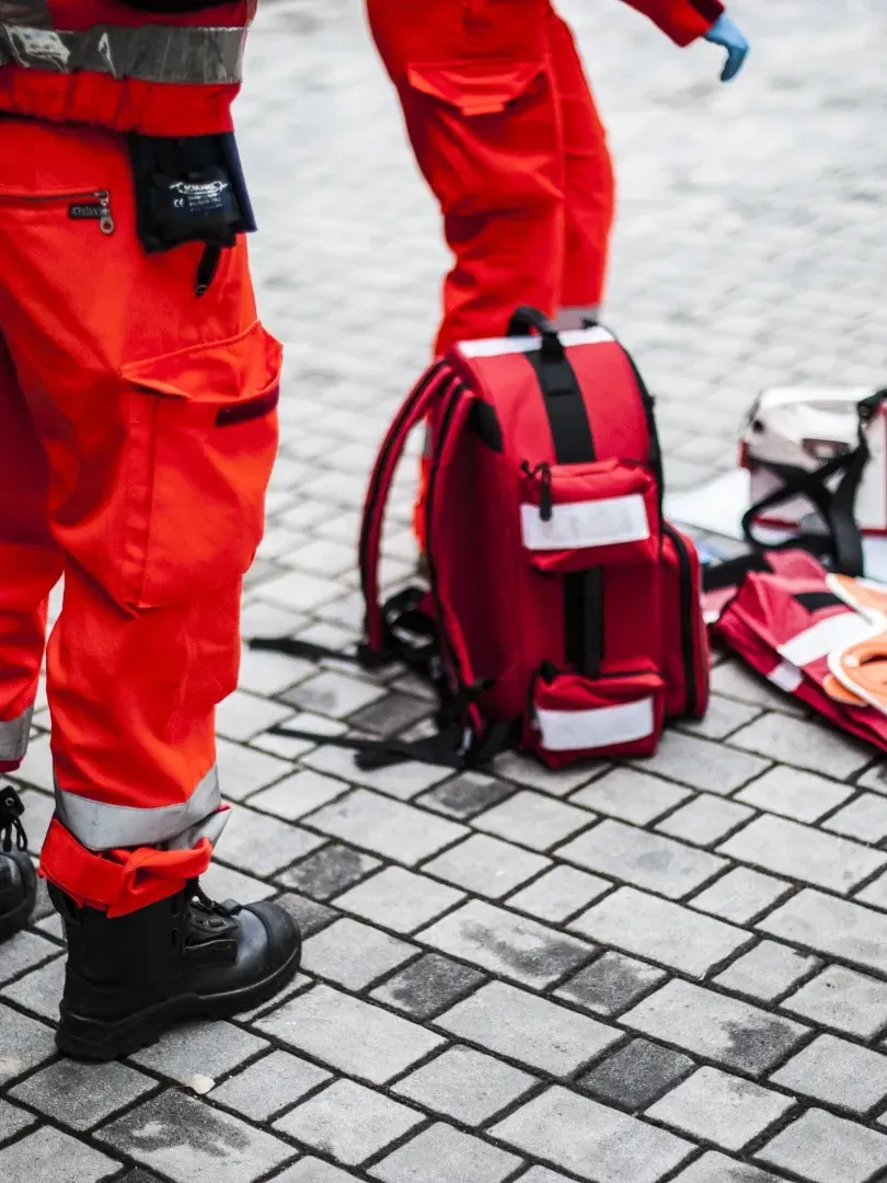 Red rescue gear and boots beside a backpack on a paved surface