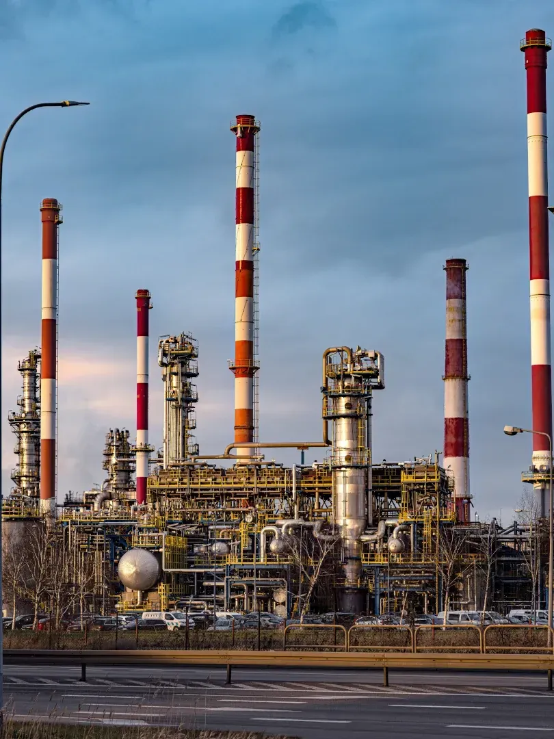 Large industrial refinery with tall red-and-white smokestacks under a cloudy sky